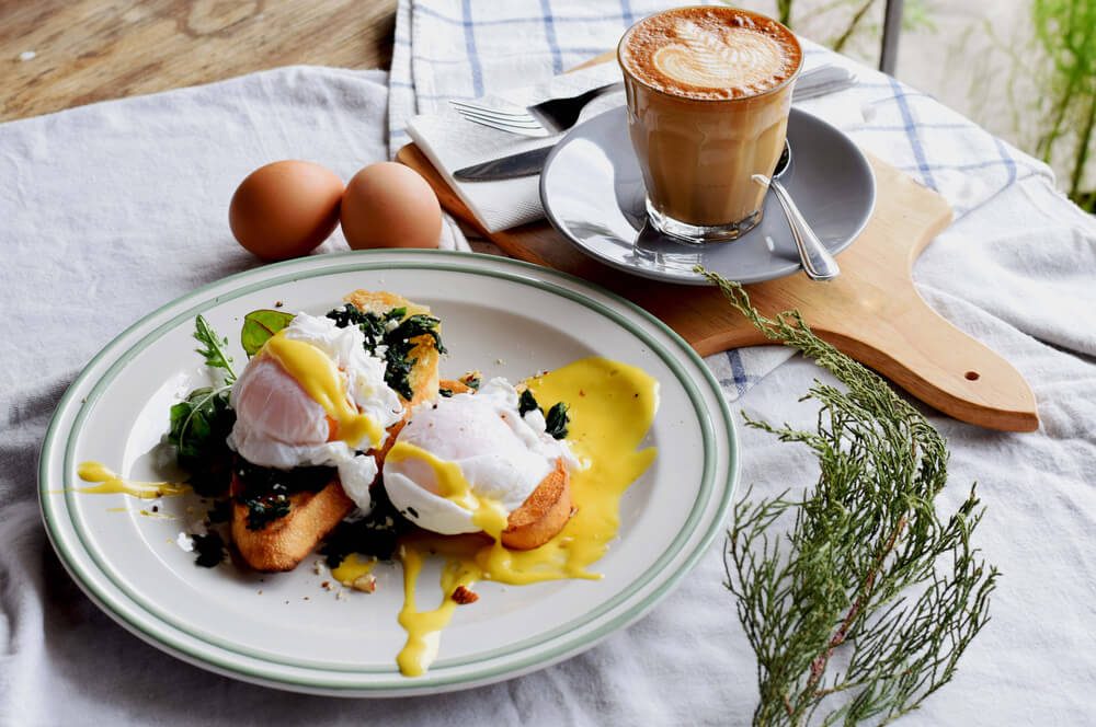 Breakfast Set, Egg benedict in white dish and a great coffee. Latte art. Wood background.