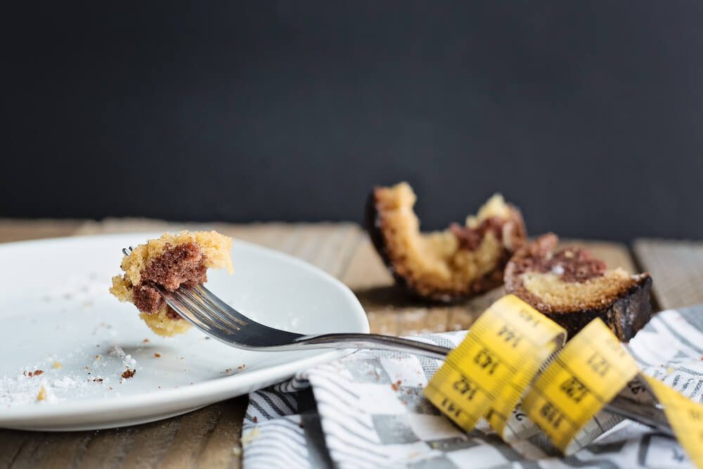piece of cake impaled on a fork with a measuring tape on a side and broken half-eaten cake at the background