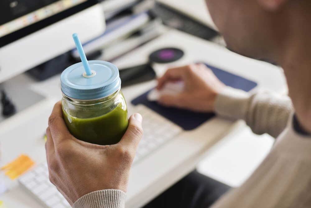 closeup of a young man drinking a green smoothie served in a glass jar at the office