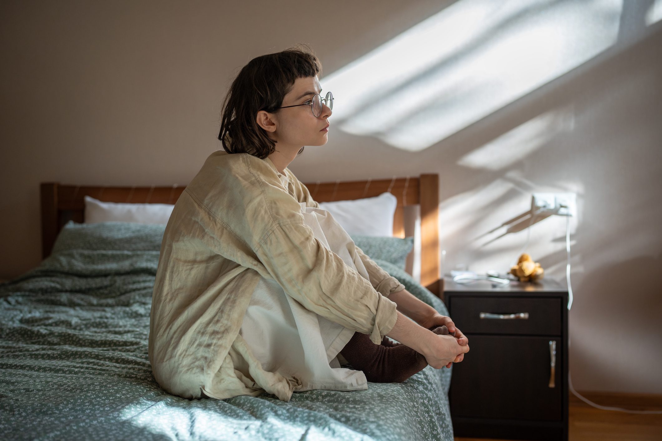 Melancholic teen girl sitting on bed in apathetical, depressed mood, thinking of misunderstanding